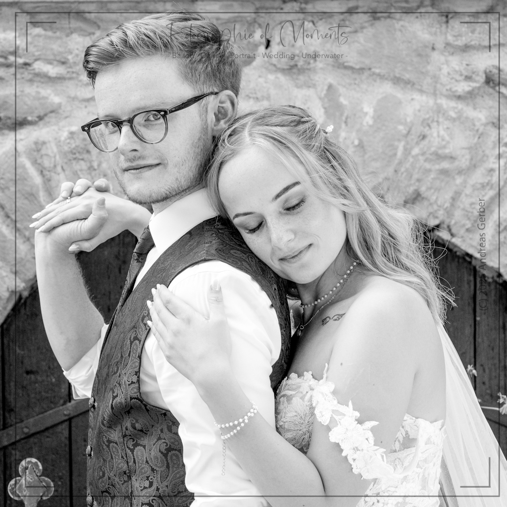 Braut umarmt Braeutigam zärtlich von hinten und legt ihren Kopf auf seine Schulter.